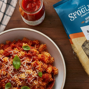 Sfoglini Classic Italian Pantry Set - Pasta dish with Garlic Radiators, tomato sauce, and basil leaves, accompanied by a jar of sauce and a package of Sfoglini pasta on a wooden table.
