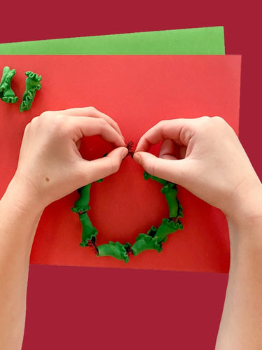 Hands making a green pasta wreath on a red background