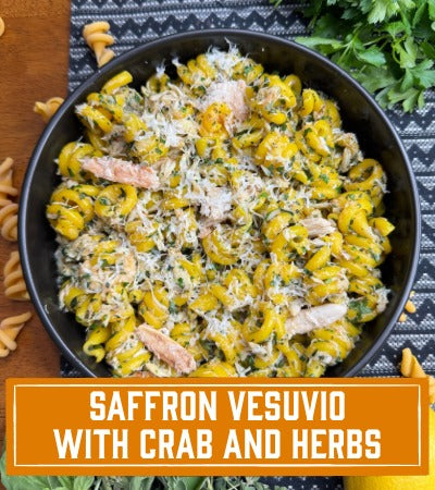 Saffron Vesuvio with Crab and Herbs in a black bowl on a wooden surface.