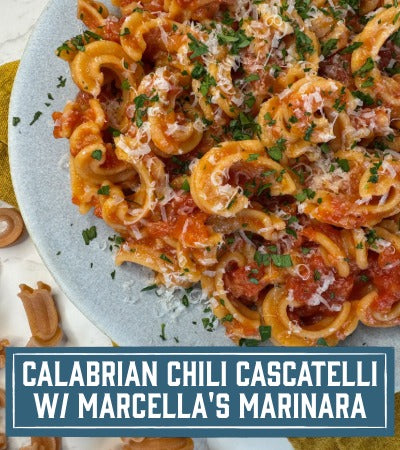 Sfoglini pasta recipe: Calabrian Chili Cascatelli with Marcella's Marinana. Plated pasta dish with tomato sauce, cheese, and herbs on a marble surface. With text overlay "Calabrian Chili Cascatelli with Marcella's Marinara" 
