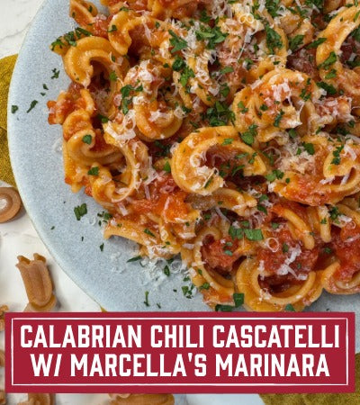 Sfoglini pasta recipe: Calabrian Chili Cascatelli with Marcella's Marinana. Plated pasta dish with tomato sauce, cheese, and herbs on a marble surface. With text overlay "Calabrian Chili Cascatelli with Marcella's Marinara" 