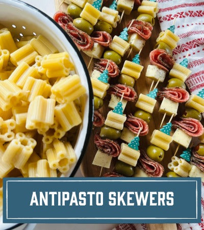 Skewers with pasta, salami, cheese. and olives next to a bowl of quattrotini pasta. With Text overlay "Antipasto Skewers"
