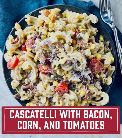 Sfoglini Pasta Recipe: Platter of Cascatelli pasta with bacon, corn, and tomatoes on a blue napkin. With text overlay "Cascatelli with Bacon, Corn, and Tomatoes"