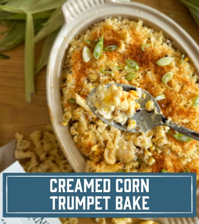 Sfoglini Pasta Recipe:  pasta in a baking dish with a spoonful being lifted, on a wooden surface. With text overlay "Creamed corn trumpet bake"