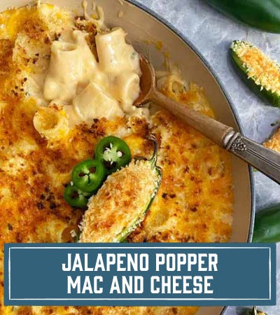 Sfoglini Pasta Recipe:  Rigatoni Jalapeno popper mac and cheese dish with a spoon in a bowl, surrounded by jalapenos. with text overlay "Jalapeno popper mac and cheese"