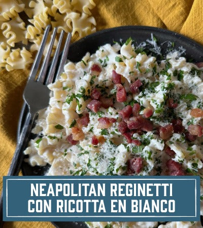 Sfoglini Pasta Recipe: Ruffled pasta with ricotta and prosciutto on a black plate with a fork, served on a yellow cloth. With text overlay "Neapolitan Reginetti con Ricotta en Bianco"