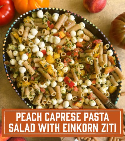 Sfoglini Pasta Recipe: Peach Caprese Pasta Salad with Einkorn Ziti in a bowl on a wooden surface. With text overlay "Peach Caprese Pasta Salad with Einkorn Ziti "