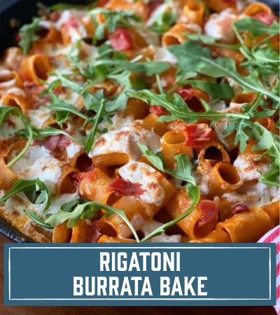 Sfoglini Pasta Recipe: bakes pasta with cheese and arugula on a wooden board. With Text overlay "Rigatoni Burrata Bake"