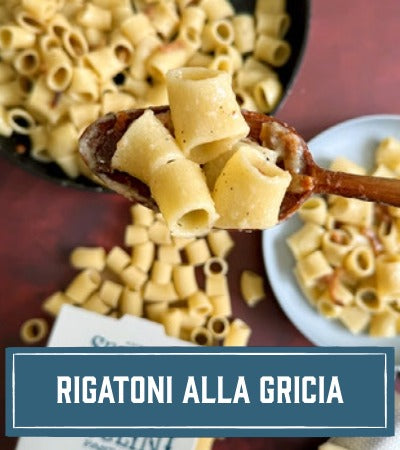 Sfoglini Pasta Recipe: Rigatoni pasta being held with a wooden spoon against a dark background. With text overlay "Rigatoni alla gricia"