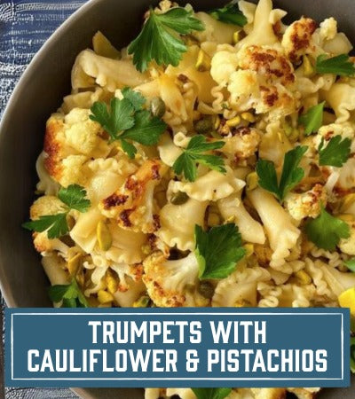 Sfoglini Pasta Recipe: Bowl of Sfoglini pasta with roasted cauliflower with pistachios and parsley on a blue checkered tablecloth. With text overlay "Trumpets with Cauliflower and pistachios"