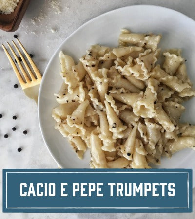 Sfoglini Pasta Recipe: Plate of Sfoglini cacio e pepe pasta with a fork on a light background. With text overlay "cacio e pepe trumpets"