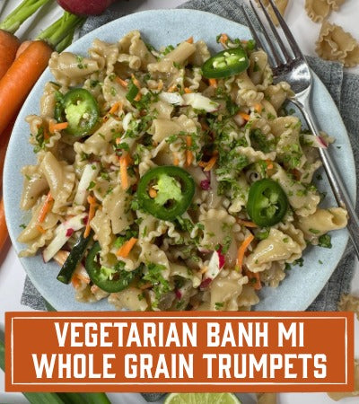 Sfoglini Pasta Recipe: Plate of vegetarian banh mi whole grain trumpets with jalapeños and carrots on a table. With Text overlay "vegetarian banh mi whole grain trumpets"