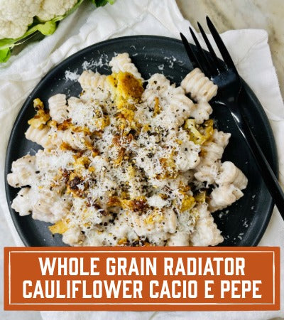 Sfoglini Pasta Recipe: Plated dish of cauliflower cacio e pepe with a black fork on a white napkin. With text overlay "whole grain radiator cauliflower cacio e pepe "
