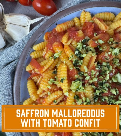 Sfoglini Pasta Recipe: Saffron Malloreddus with Tomato Confit. Golden pasta on a blue plate with red sauce.