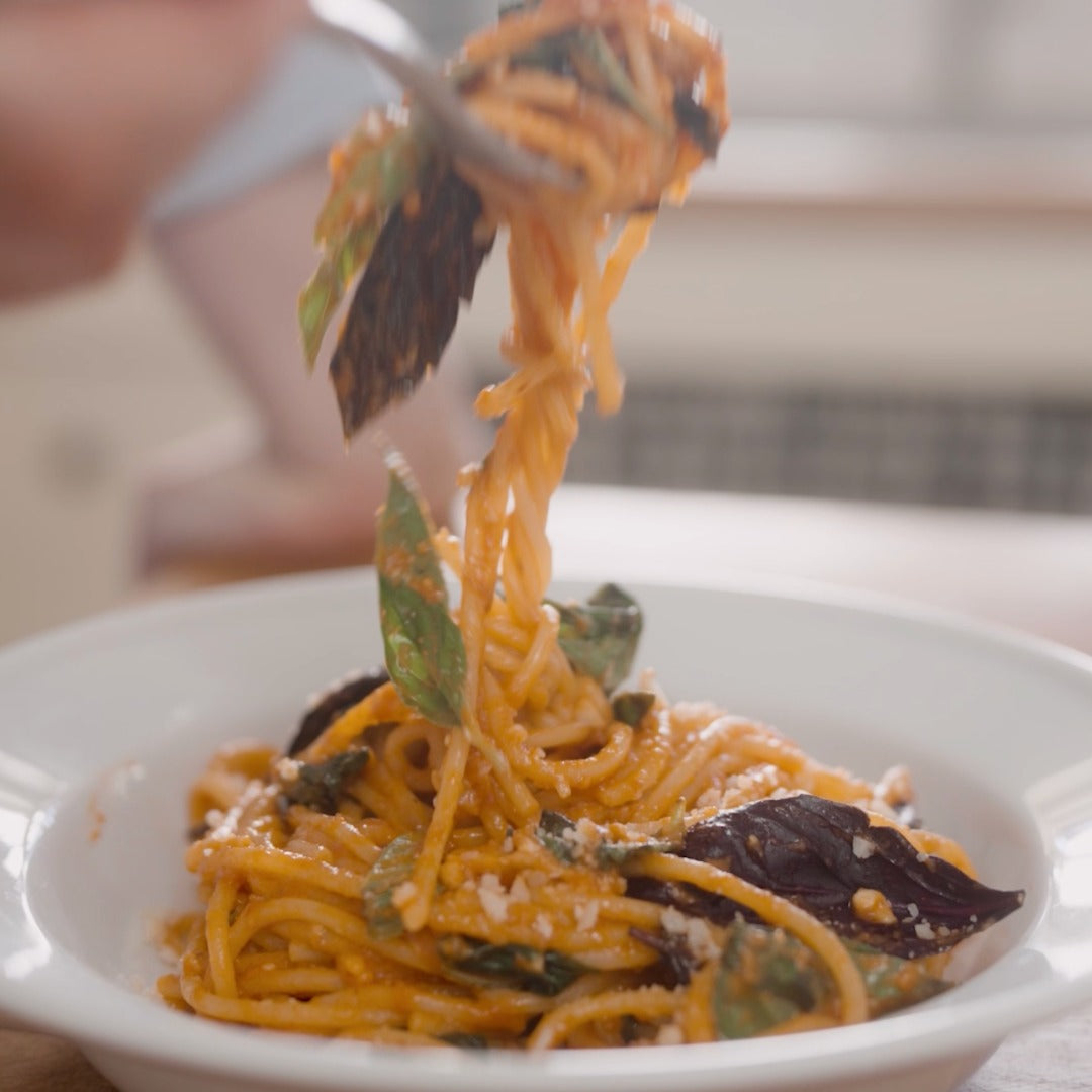 Six Seasons of Pasta Cookbook & Pasta Set - Pasta with basil leaves on a white plate, being lifted with a fork.